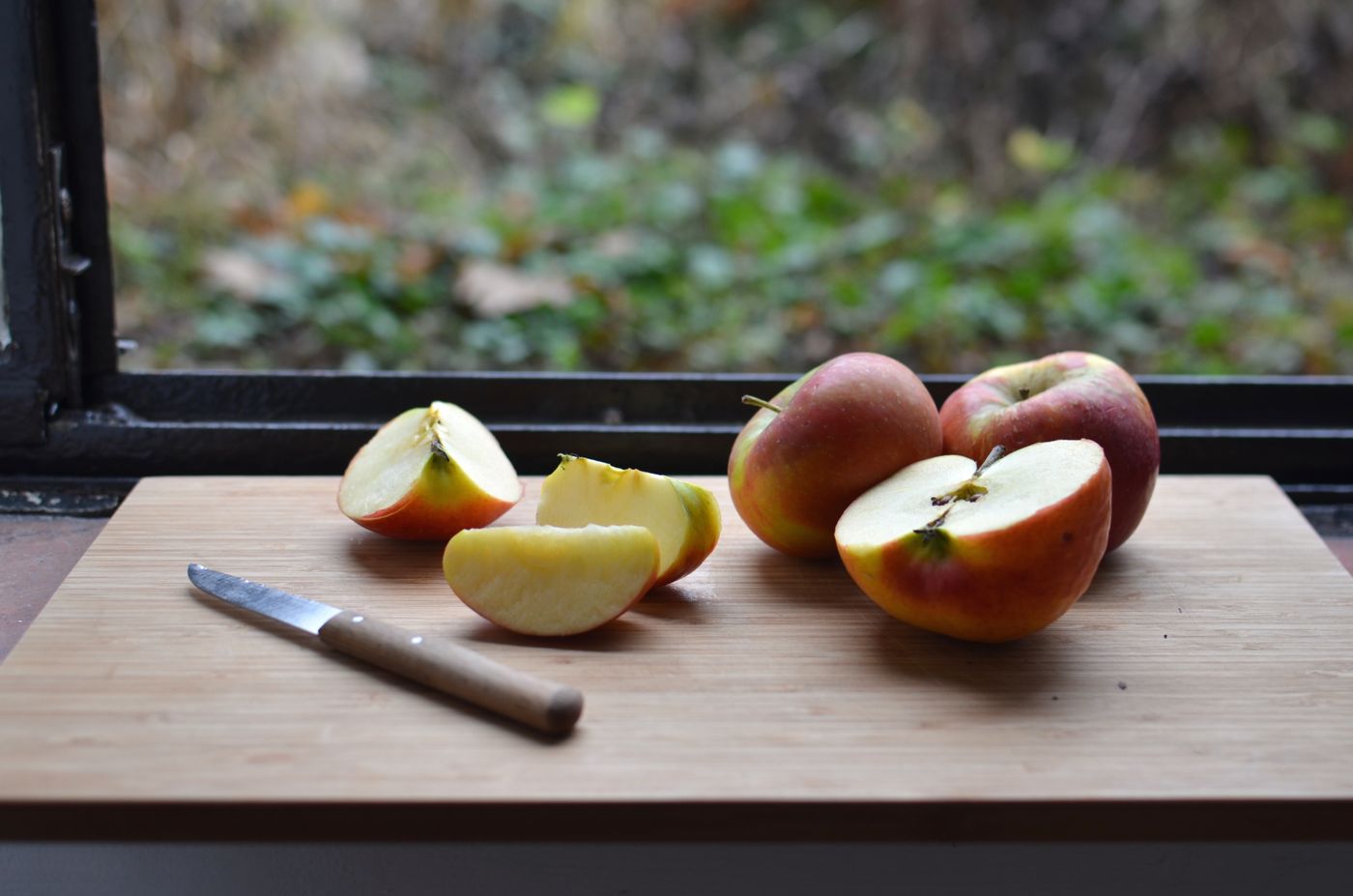 Cut red apples and a knife on a wooden board beside a kitchen window