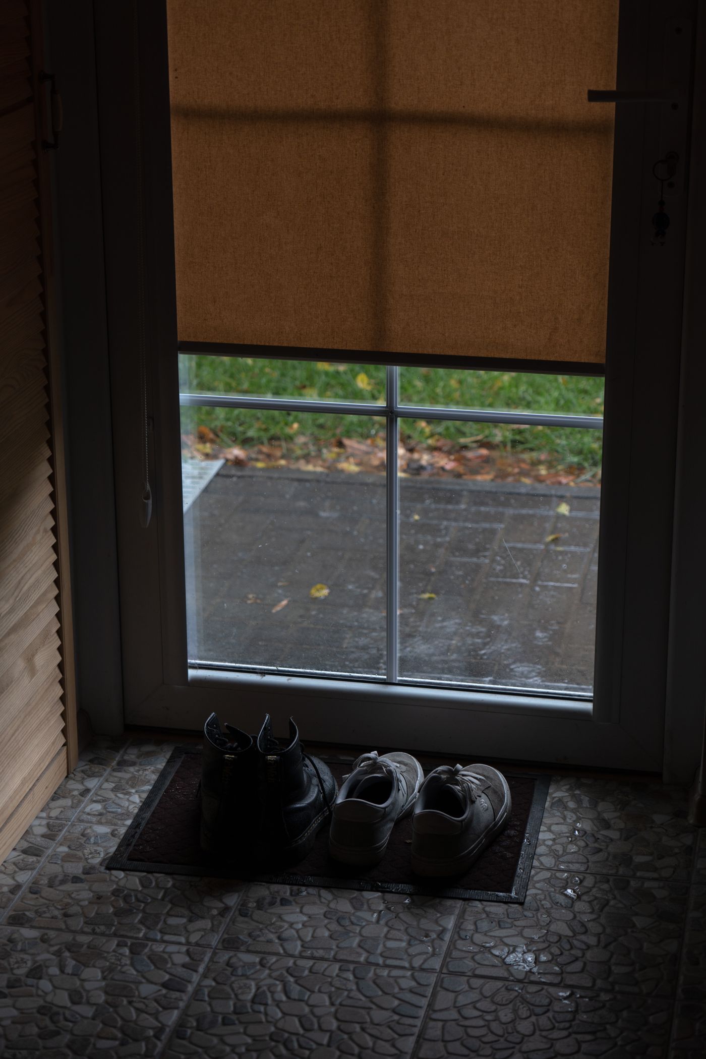 Shoes on a mat beside an entry door on a rainy day