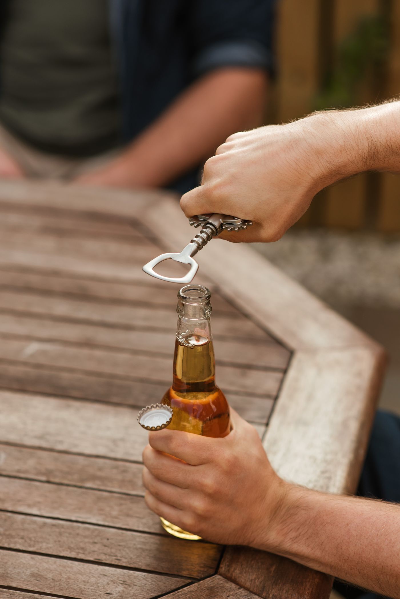 Hands using an opener to remove a cap from a glass beverage bottle