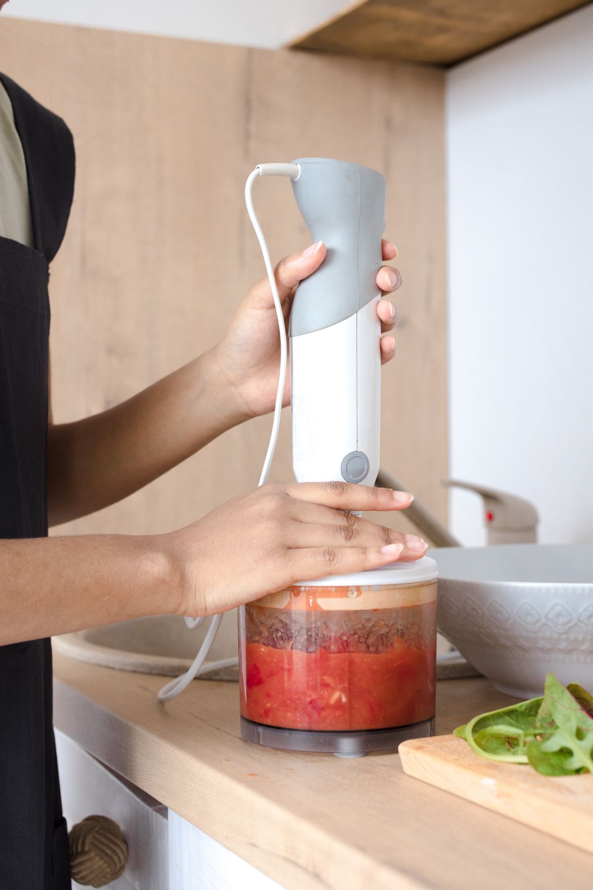 Person blending vegetables with a hand blender