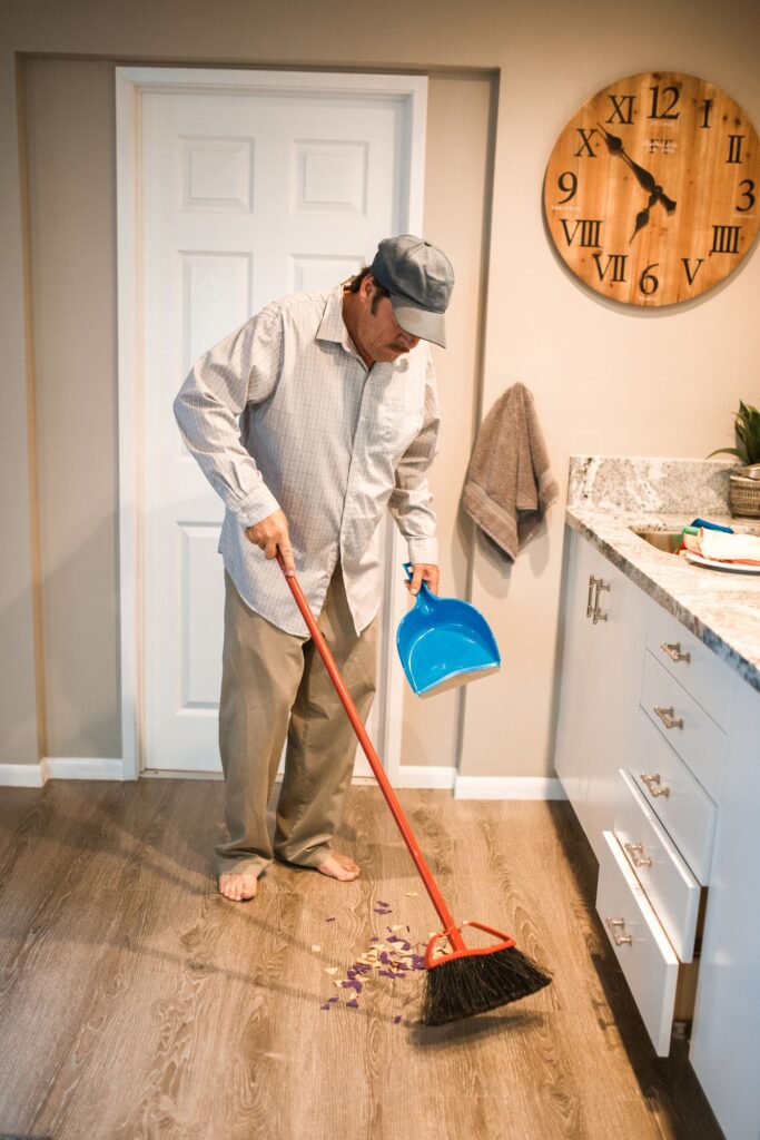 Person sweeping a kitchen floor with a broom and dustpan