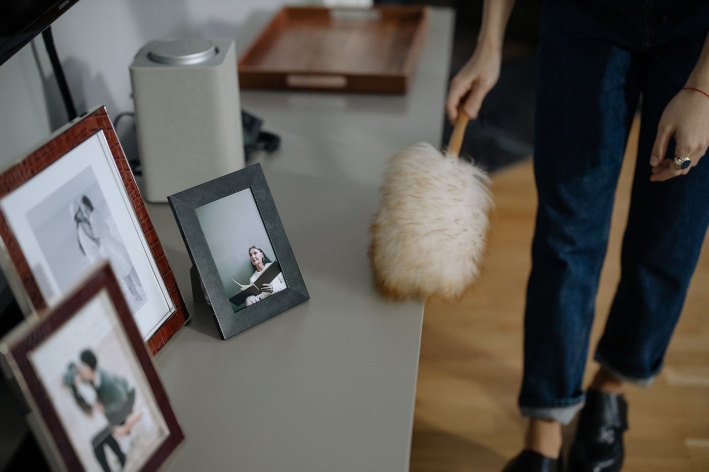 Person dusting a shelf with framed pictures