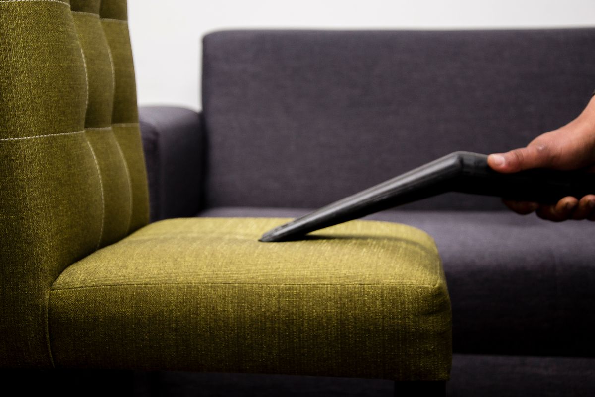 Person cleaning a sofa chair with a handheld tool
