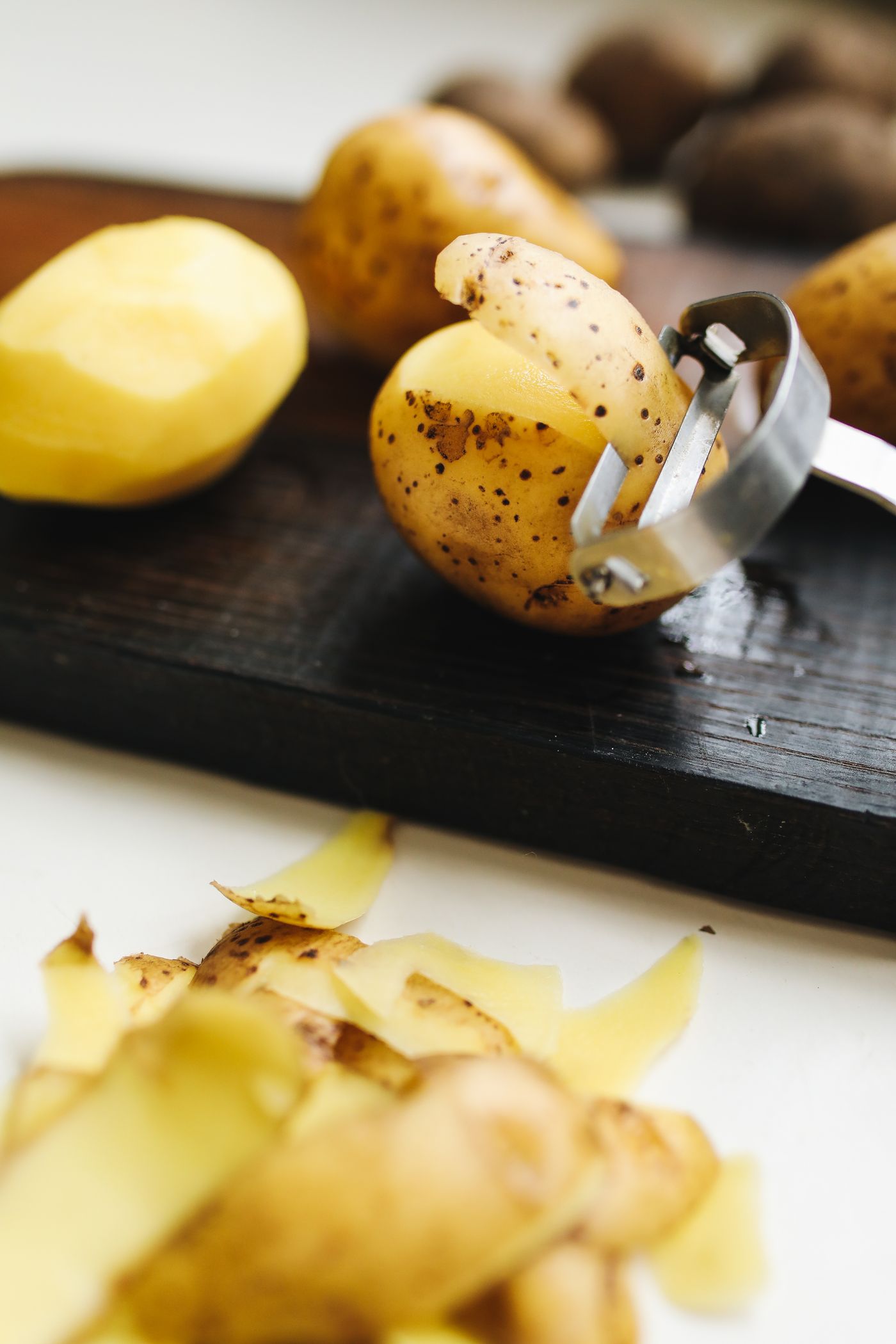 Potatoes and a peeler on a wooden board