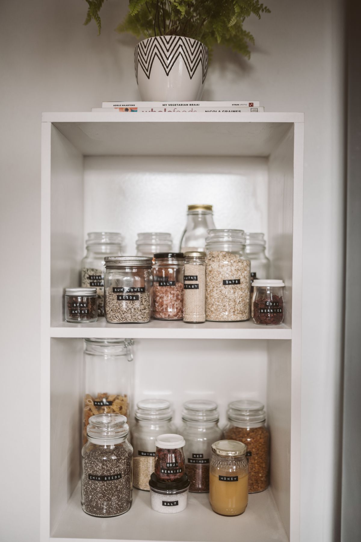 Labeled glass jars holding dry foods on white pantry shelves