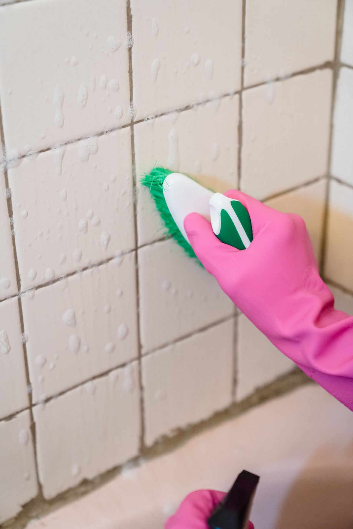 Person scrubbing bathroom wall tiles with a brush
