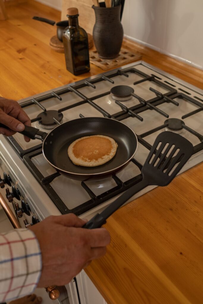 Hands holding a pan and spatula while cooking