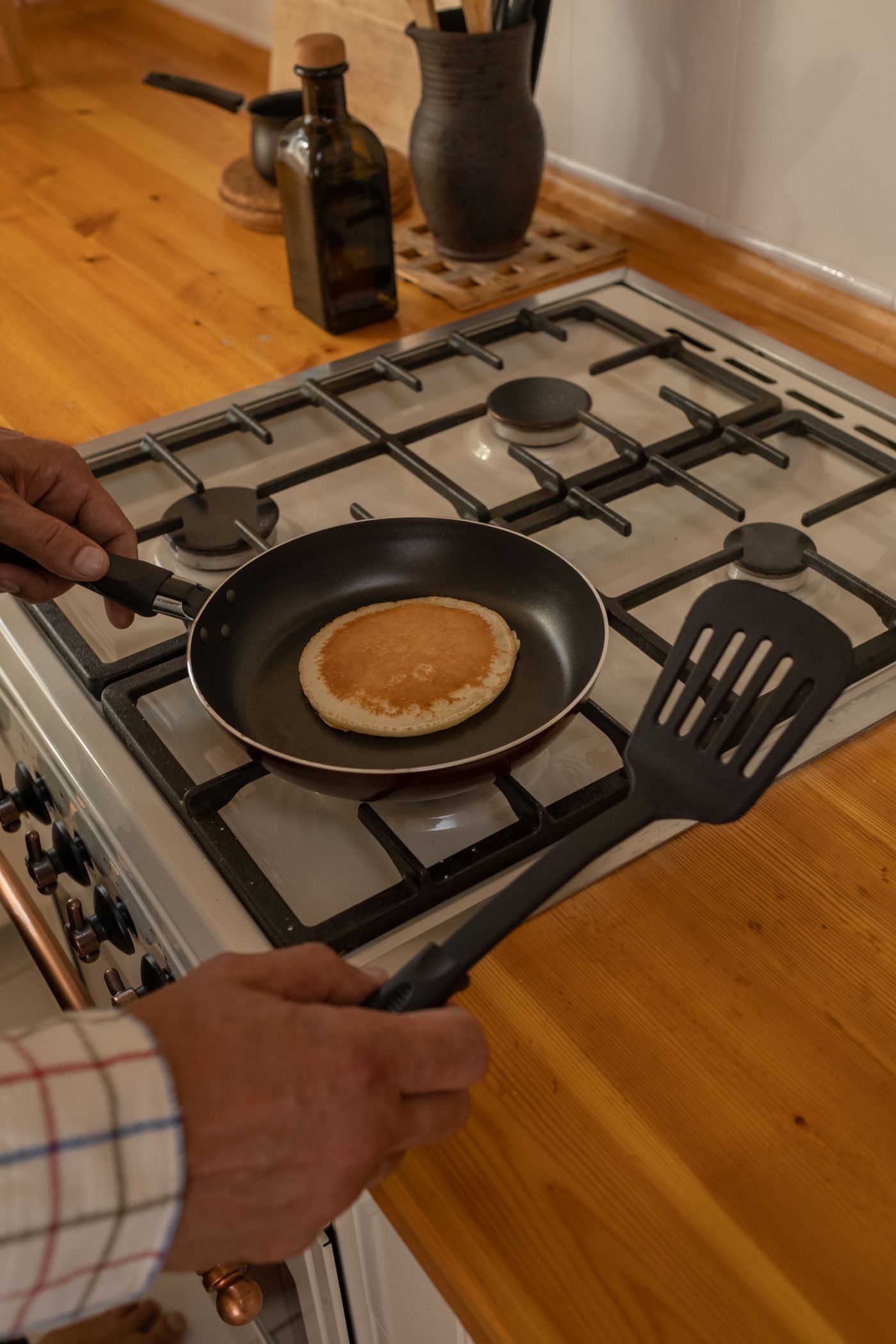 Hands holding a pan and spatula while cooking