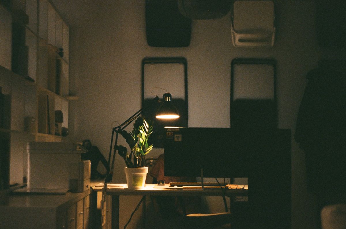 Lit desk lamp beside a computer and plant