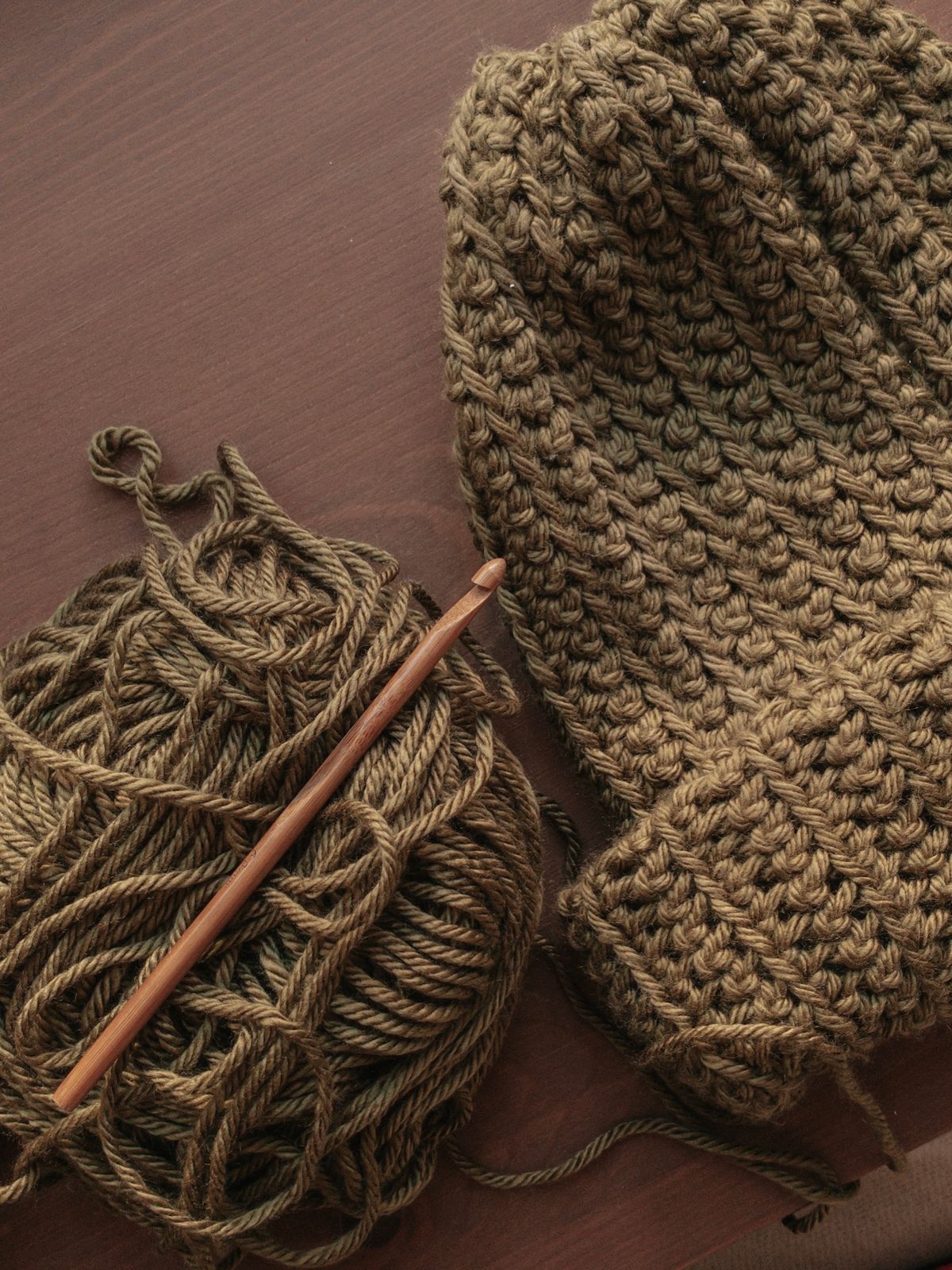 Yarn, a crochet hook and a handmade hat on a wooden table